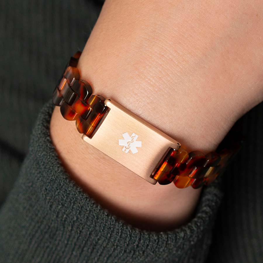 Woman wearing green sweater with back of wrist turned to display closed rose gold clasp on resin medical ID bracelet. 