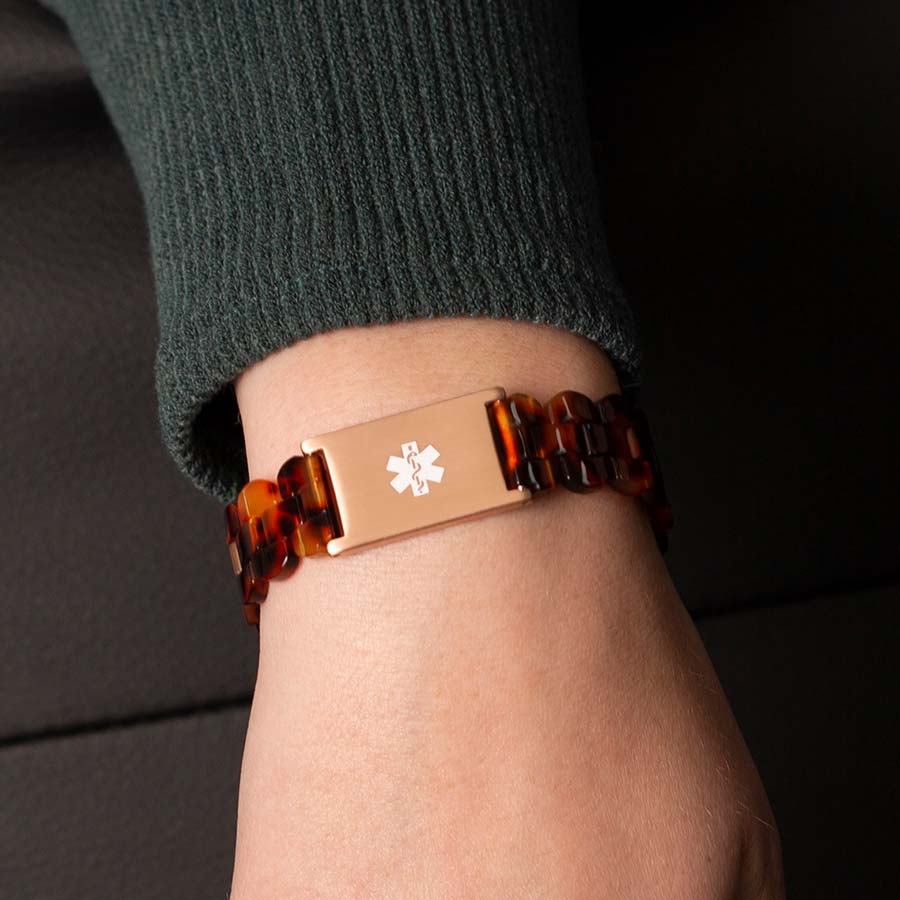 Woman wearing green sweater with back of wrist turned to display closed rose gold clasp on resin medical ID bracelet. 