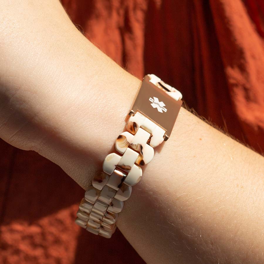 Woman displays stylish rose gold and cream medical ID bracelet with white medical symbol on her wrist.