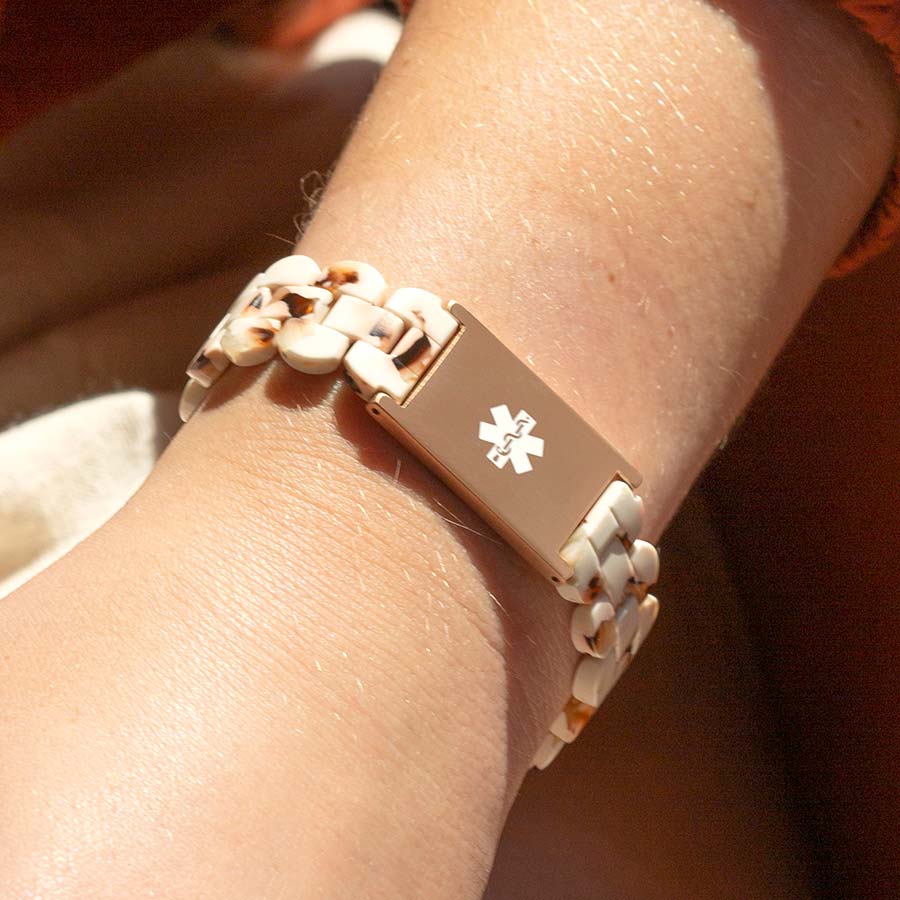 Woman wearing rose gold and cream medical ID bracelet with white medical caduceus symbol.