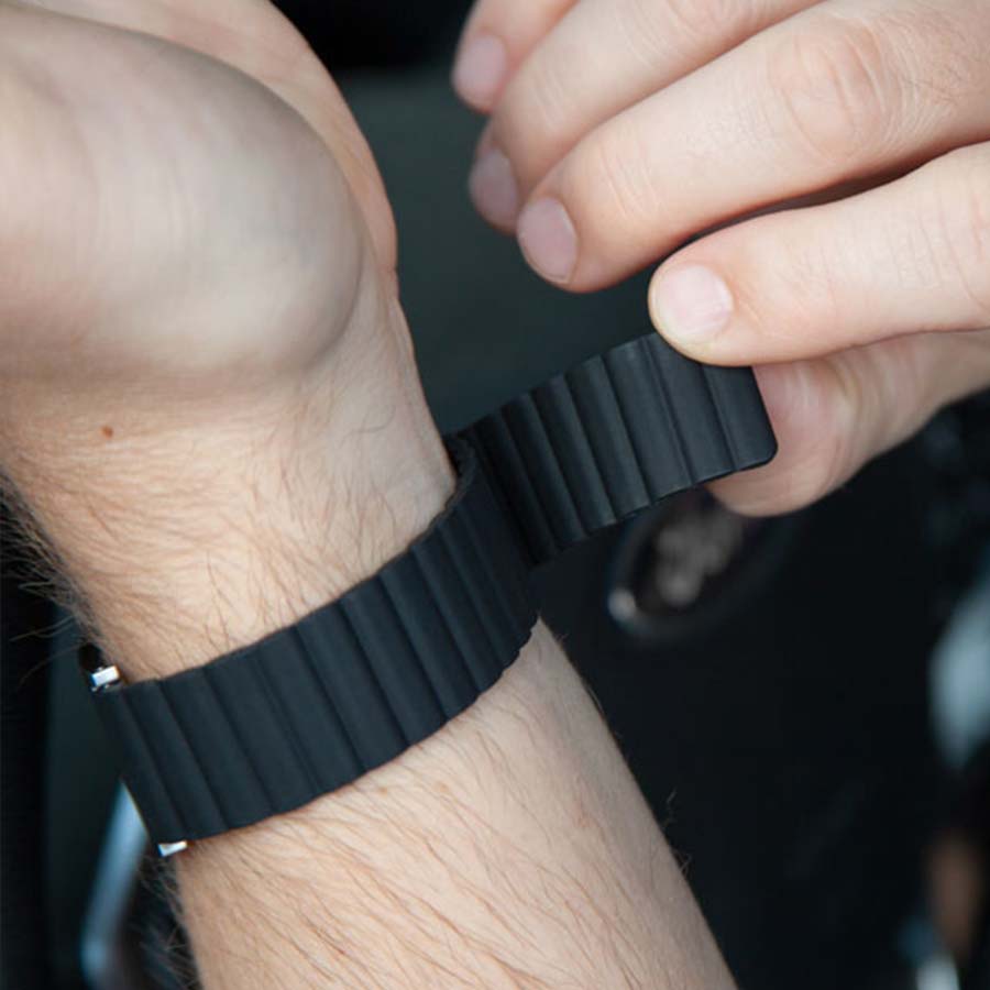 Man adjusts clasp-free magnetic band on black silicone medical ID bracelet.