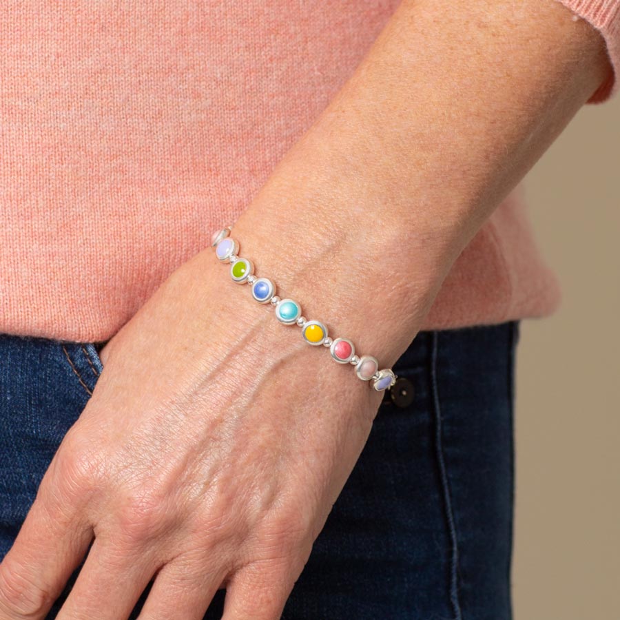 Woman in pink sweater and dark denim wearing silver tone colorful enamel inlay beaded stretch bracelet.