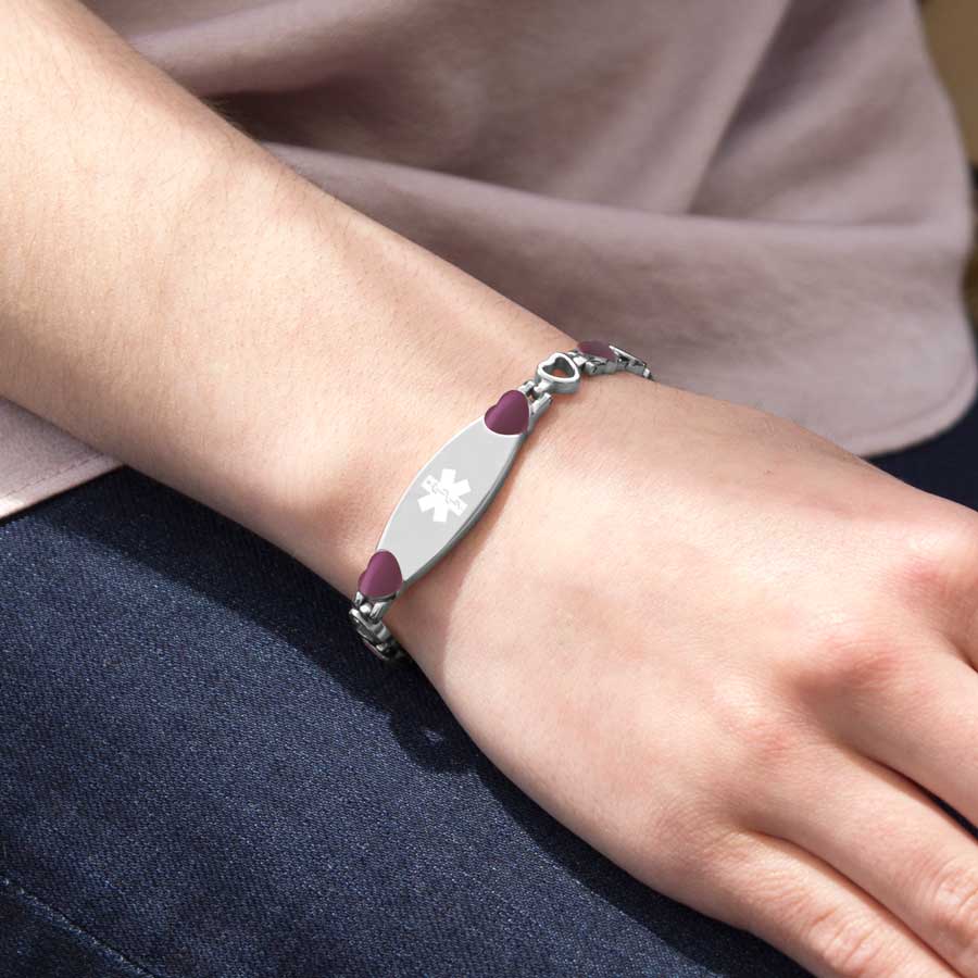 Woman wearing burgundy tone and and stainless steel heart link bracelet with attached medical ID tag with white medical symbol.