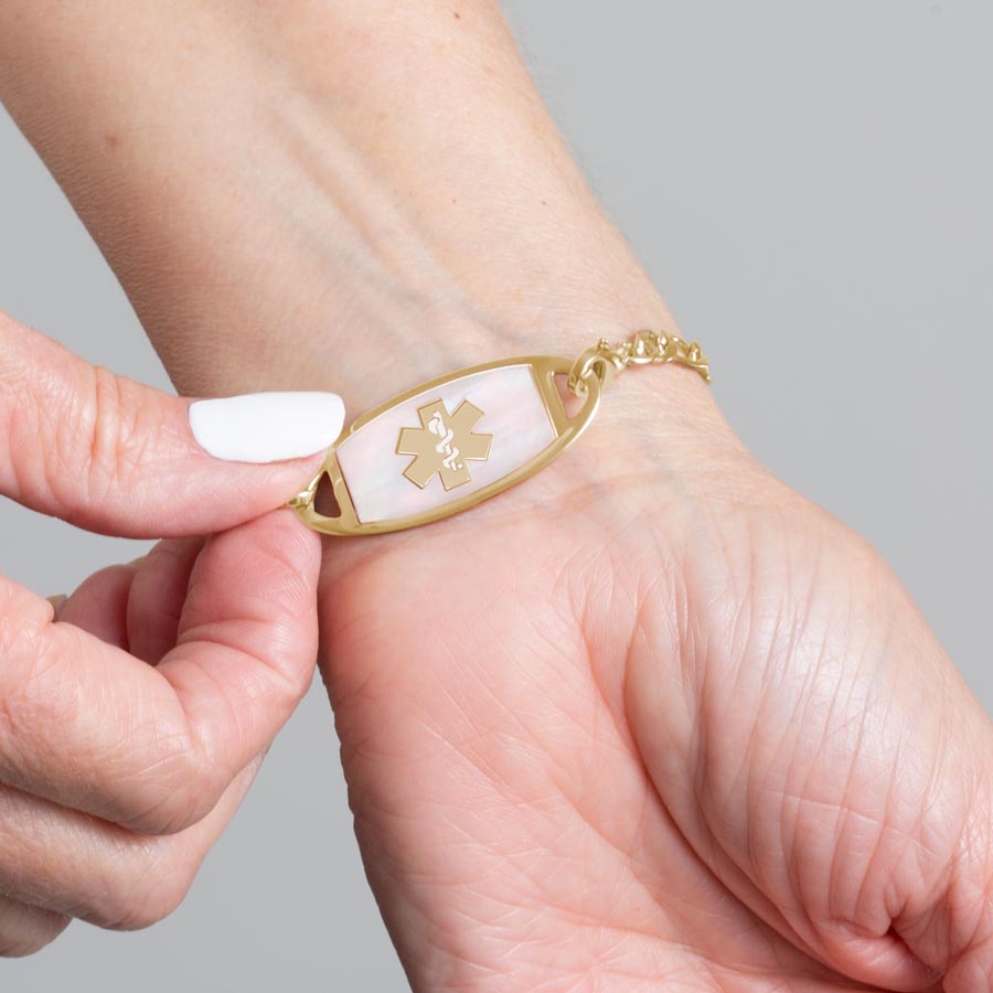 Woman showing gold and mother of pearl medical ID tag with gold medical caduceus symbol