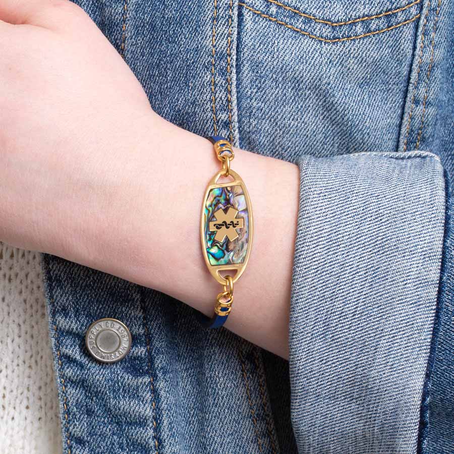 Woman in denim jacket wearing navy blue metallic leather bracelet and gold tone natural abalone inlay med ID tag.