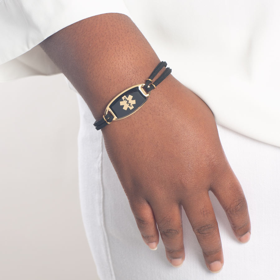 Woman wearing gold medical ID bracelet with black suede