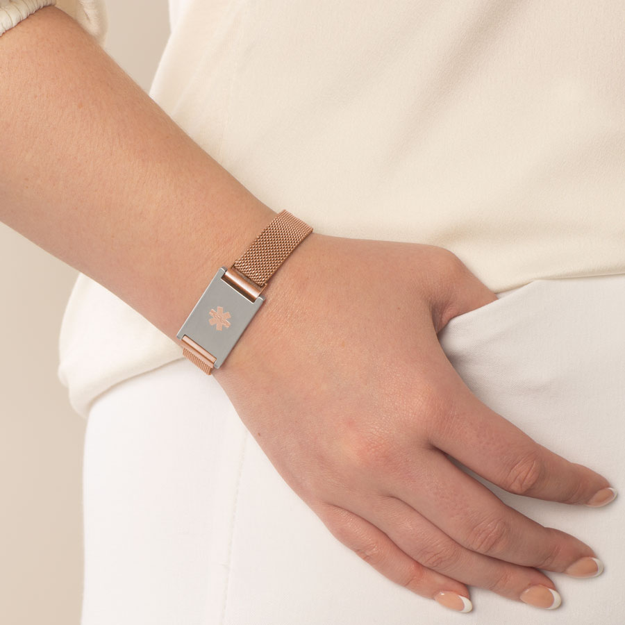 Woman wearing rose gold tone stainless steel mesh band with stainless steel medical ID tag with rose gold tone medical symbol.