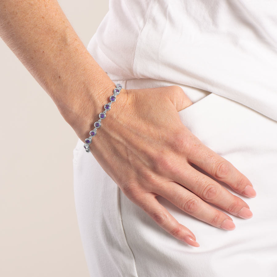 Woman wearing silver tone medic alert bracelet with round violet color cubic zirconia crystals.