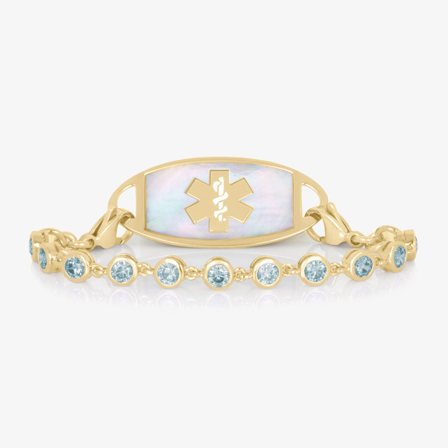 12k gold plated tennis bracelet with individually linked, round, aquamarine cubic zirconias. Attached to a gold tone Mother or Pearl inlaid medical ID tag.