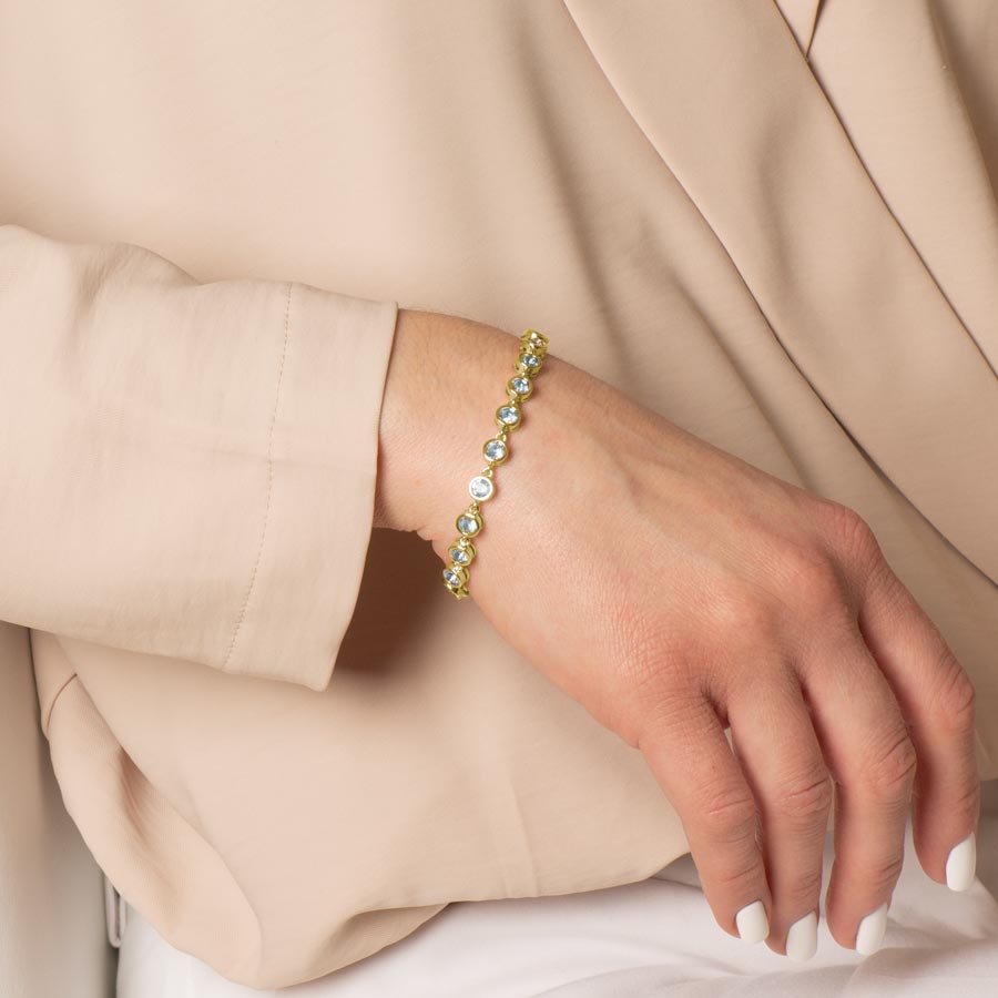 Woman wearing a bracelet featuring individually linked, round, aquamarine cubic zirconias