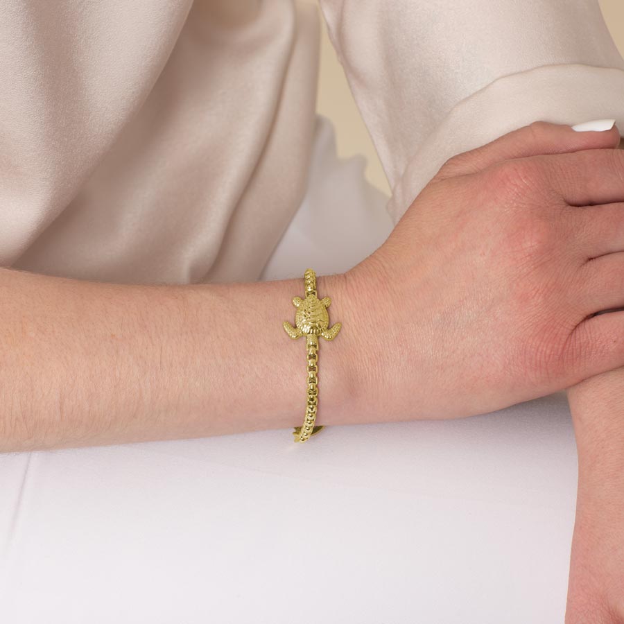 Model wearing a gold tone box chain bracelet with sea turtle centerpiece.