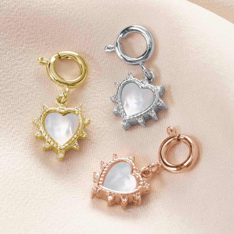 Three heart shapped charms are displayed on silky fabric in rose gold, silver and gold tones.