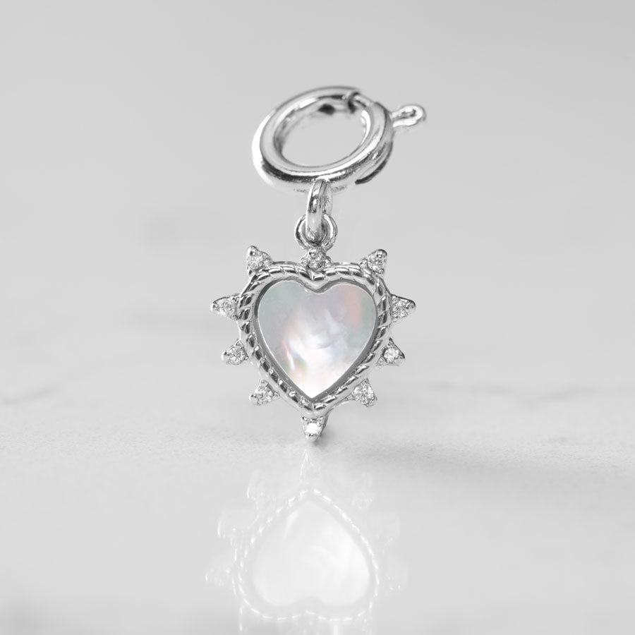 The moth of pearl inlay glows on a silver heart shaped charm, accented with crystals on a white marble counter