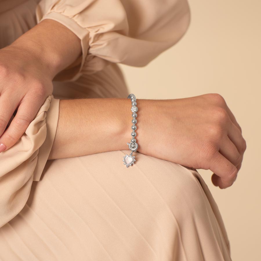 Elegant woman wearing a silver heart charm on her bracelet.