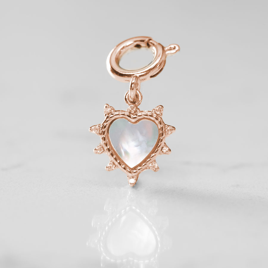 The mother of pearl inlay glows on a heart shaped charm in rose gold on a white marble counter.