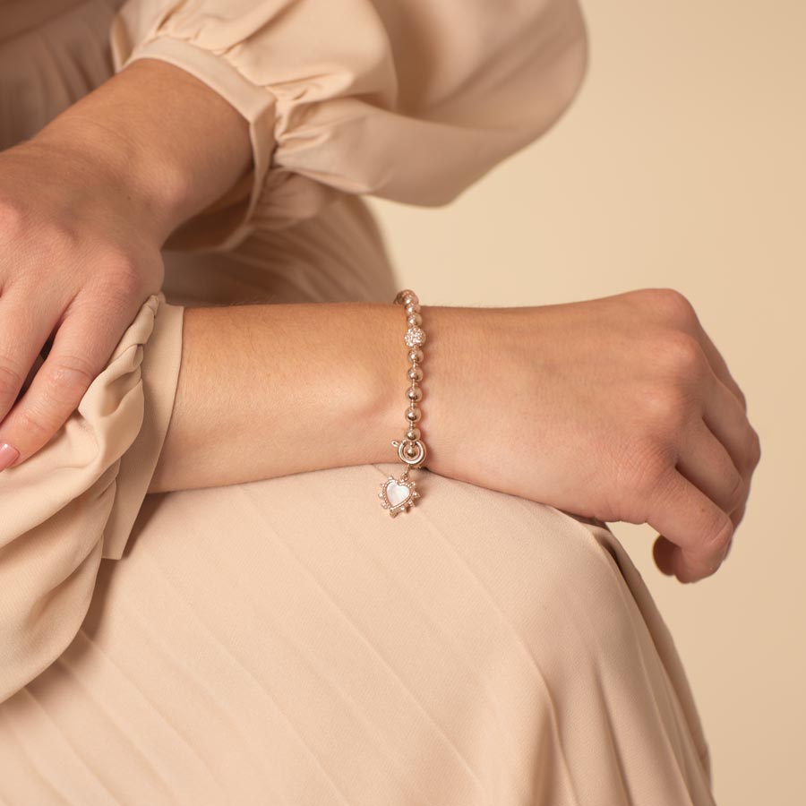 Lovely woman wearing a heart shaped, rose gold charm with mother of pearl inlay and crystal border.