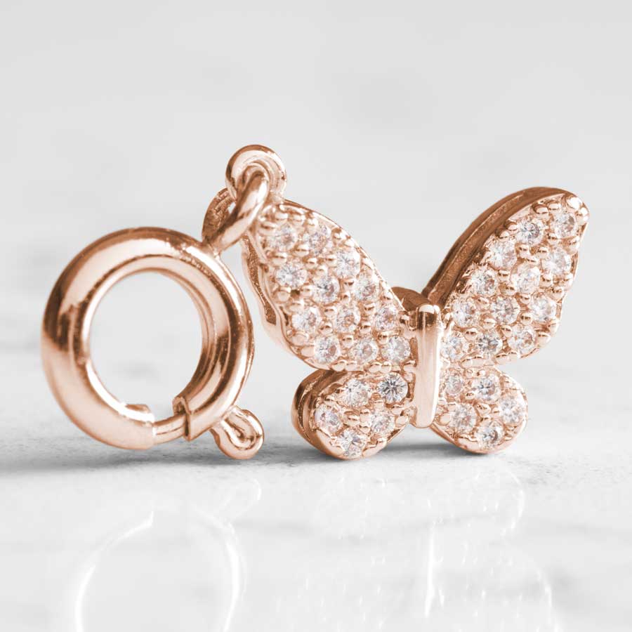 Crystal in lays sparkle on a rose gold, butterfly shaped charm, sitting atop white marble.