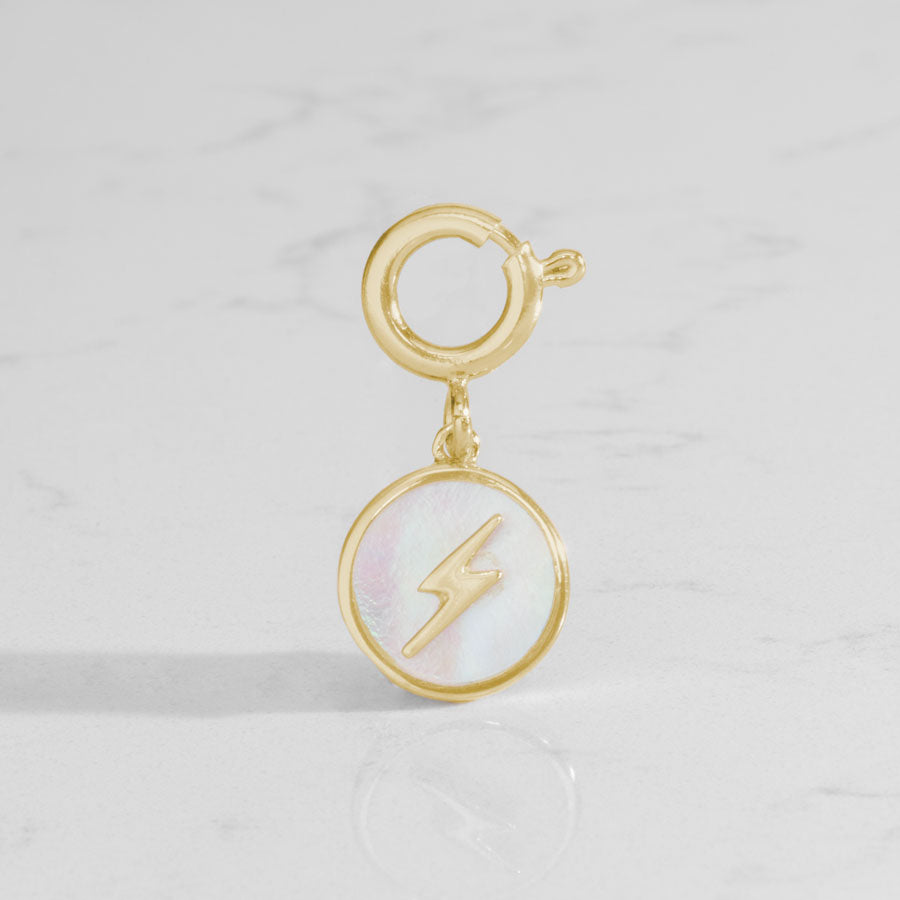 Round, gold tone charm, featuring a mother of pearl inlay with gold lightning bolt.