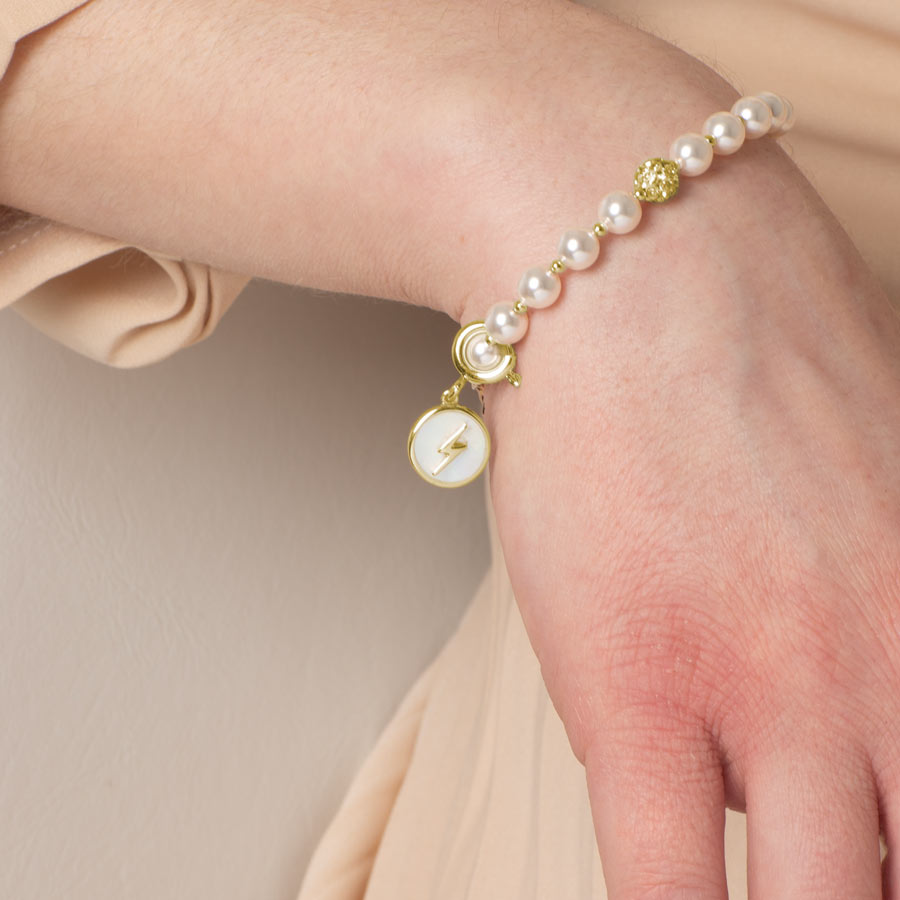 Woman wearing gold tone lightning bolt and mother of pearl charm on her medical ID bracelet.