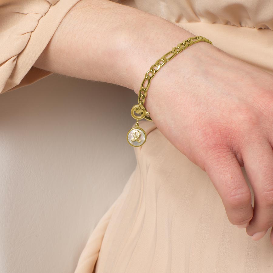 Woman wearing round gold tone charm with mother of pearl inlay and Gold tone, crystal set ribbon.