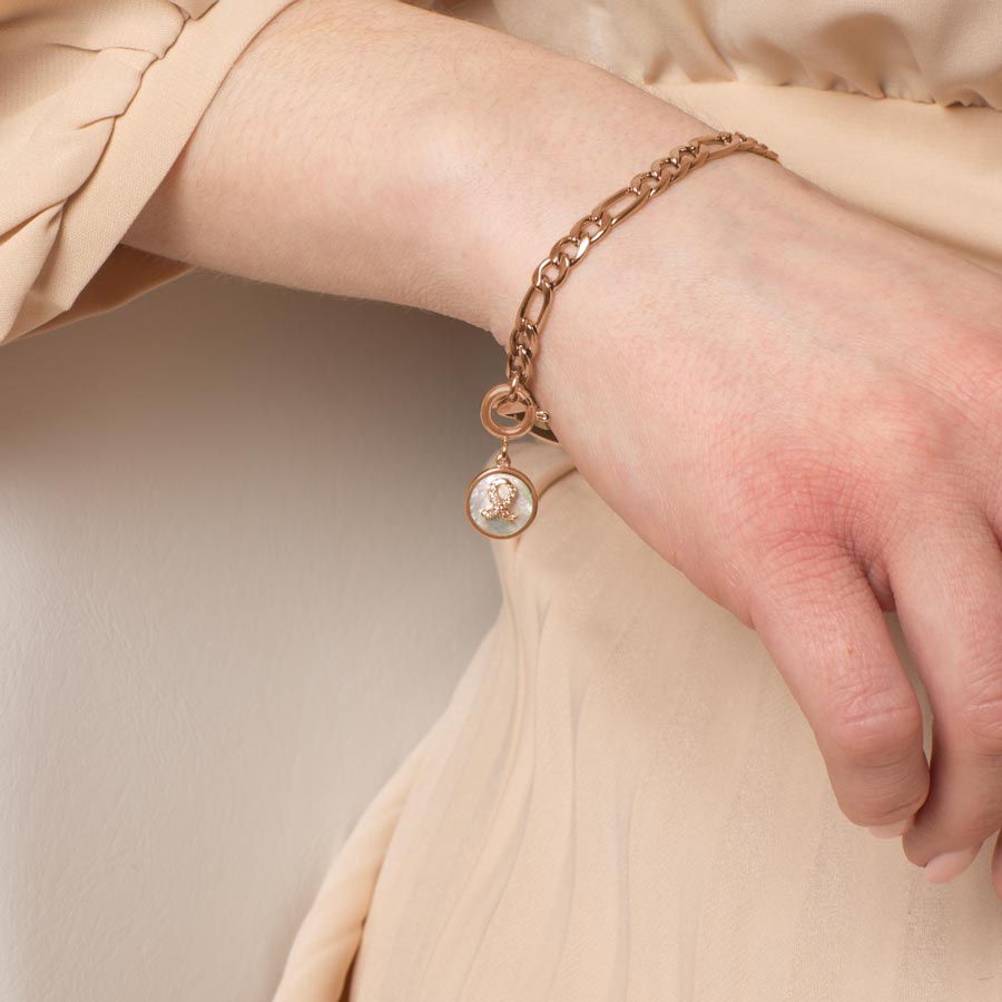 Woman wearing round rose gold tone charm with mother of pearl inlay and rose gold tone, crystal set ribbon.