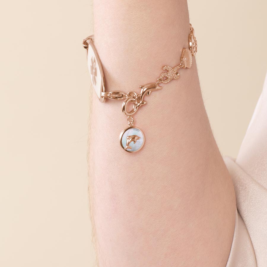 Woman wearing a rose gold, mother of pearl inlaid, dolphin charm.