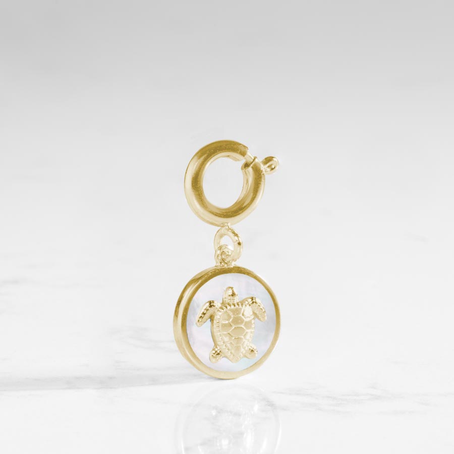 The mother of pearl inlay shines behind a gold tone sea turtle on this circle shaped charm.