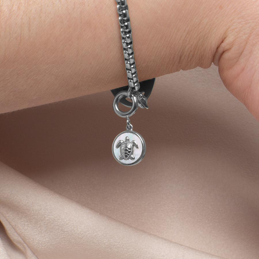 Woman wearing silver sea turtle charm with inlaid mother of pearl.