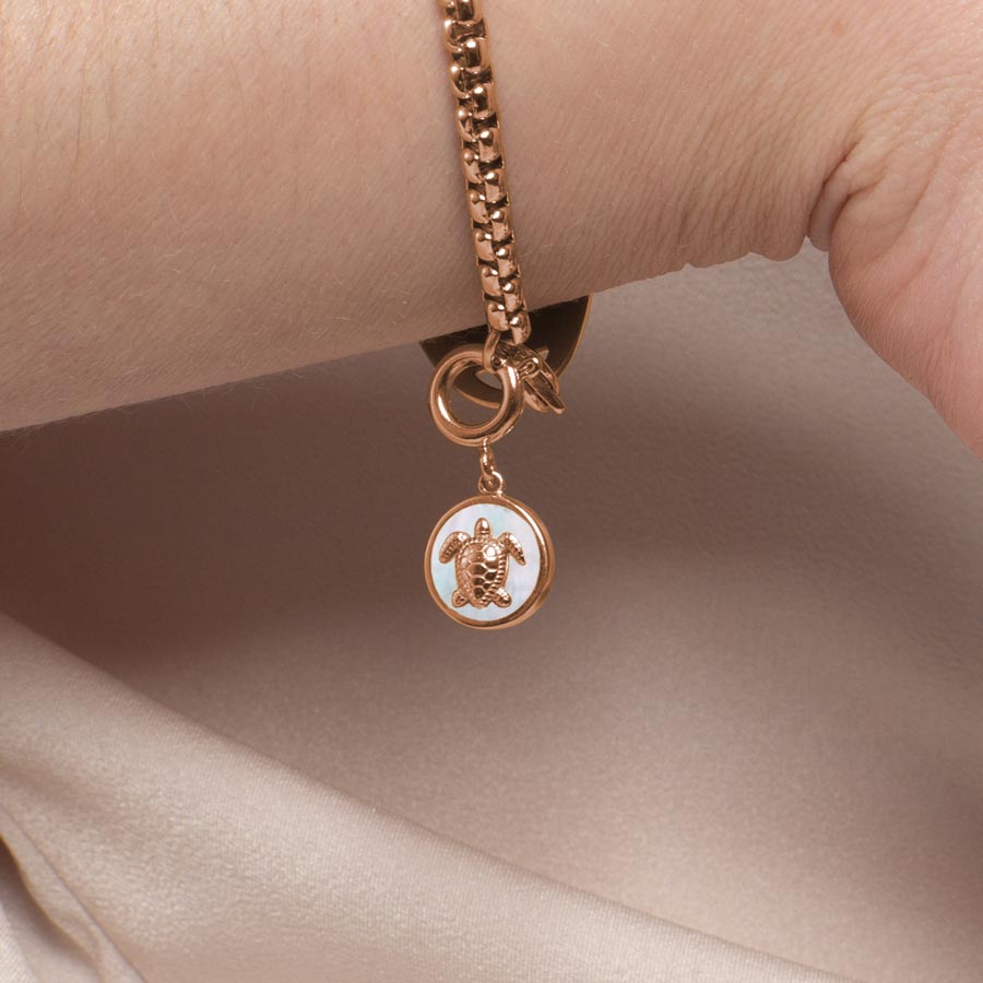 Woman wearing rose gold, round, sea turtle charm with mother of pearl inlay.