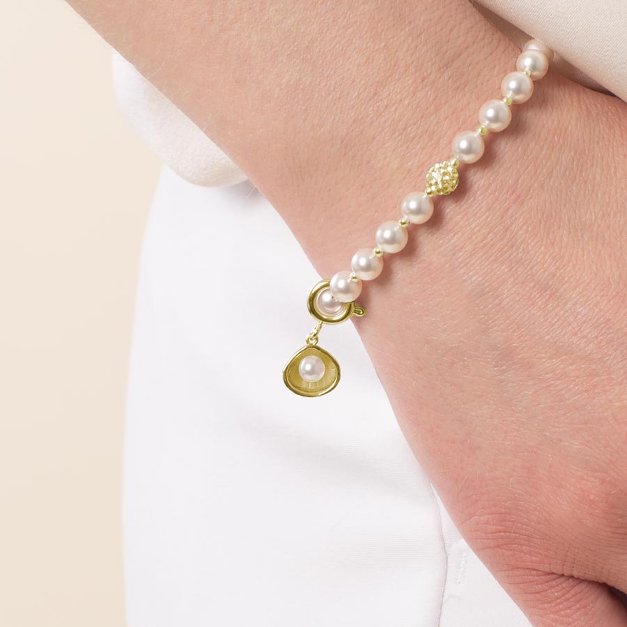 Woman wearing gold toned open oyster shell charm featuring a single pearl.