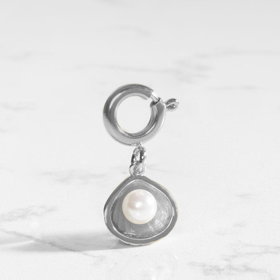 Sterling silver open oyster shell charm featuring a single, lustrous pearl, displayed on white marble table.