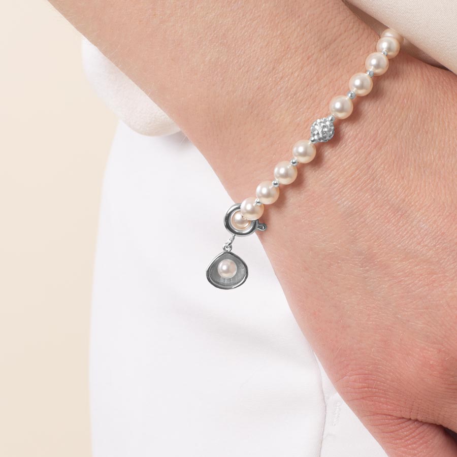 Woman wearing a sterling silver open oyster charm featuring a single, lustrous pearl.