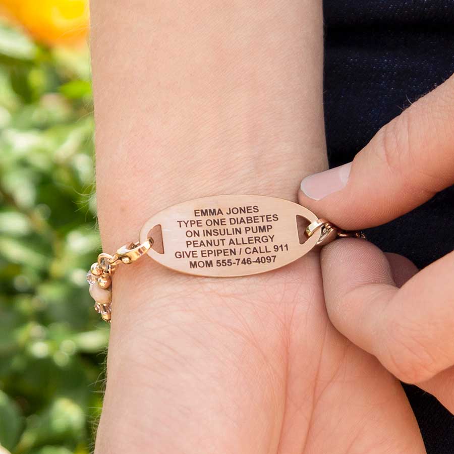 Woman wearing blush and rose gold tone beading bracelet showing premium laser engraving outside with green bush in background.