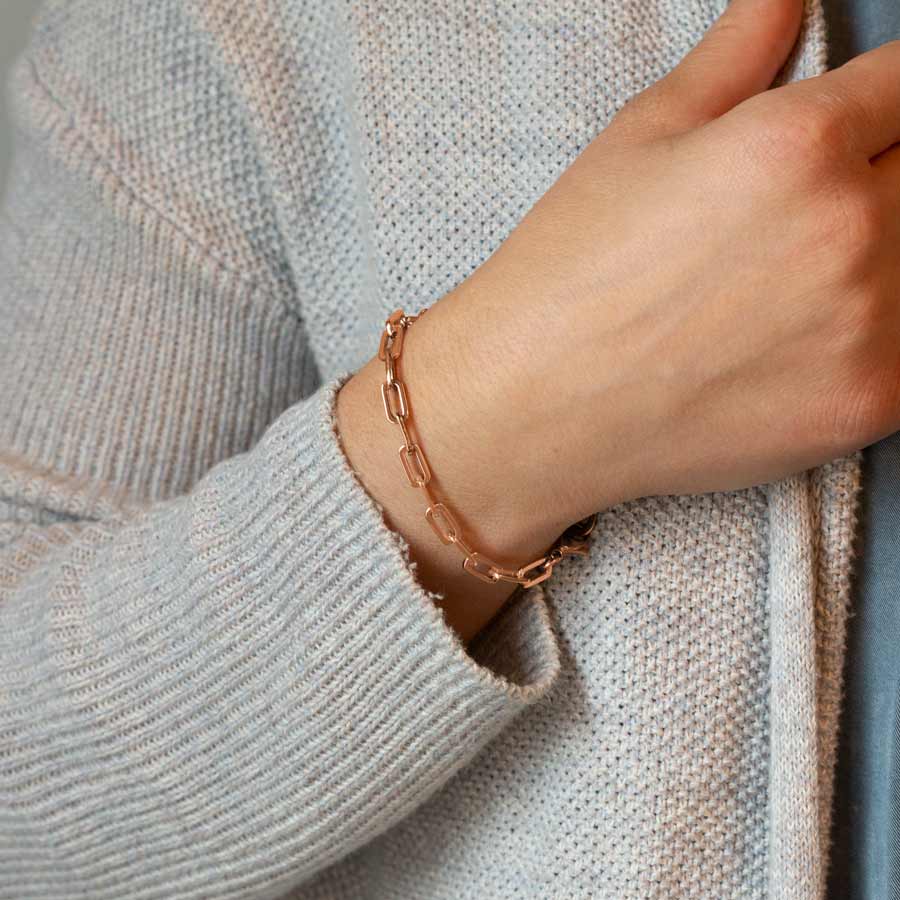 Woman grasping sweater wearing rose gold medical ID bracelet in rose gold paperclip chain