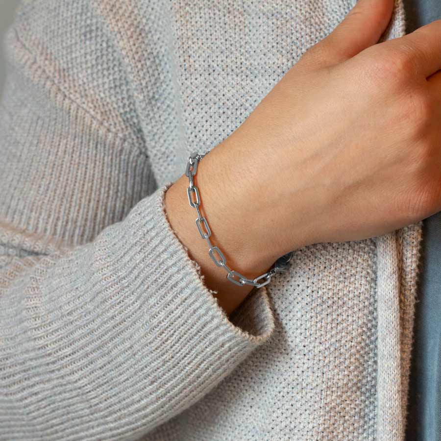 Woman grasping sweater wearing silver medical ID bracelet in silver paperclip chain