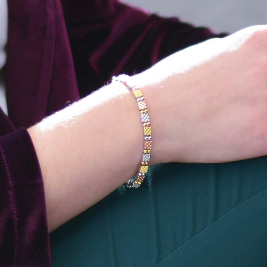 Woman sitting wearing 12k gold plated, silver tone, and rose gold tone link chain bracelet. 