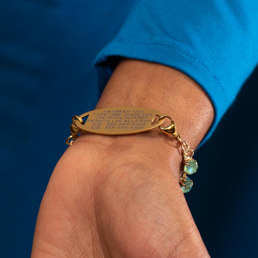 Woman in blue top wearing 12 karat gold plated bracelet showing premium laser engraving on gold tone ID tag.