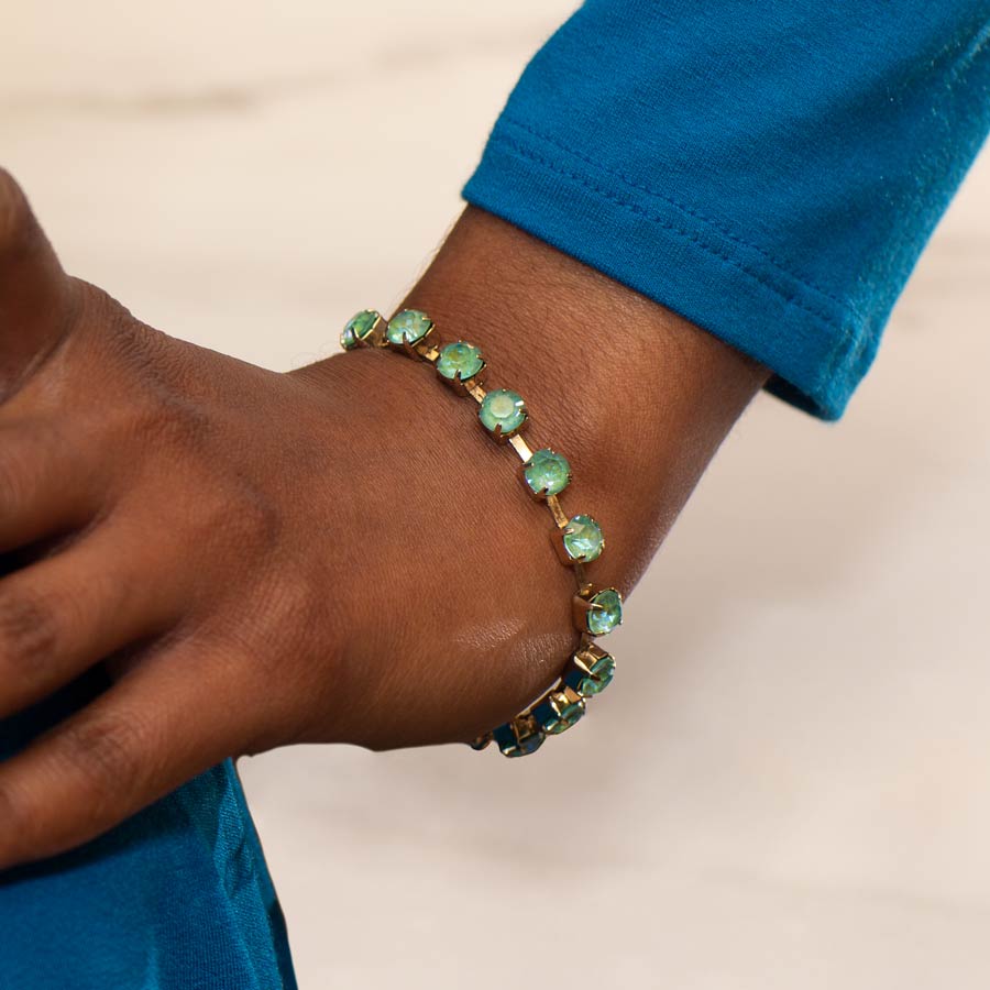 Woman in blue top with hand on hip wearing 12 karat gold plated bracelet with sea green crystals.