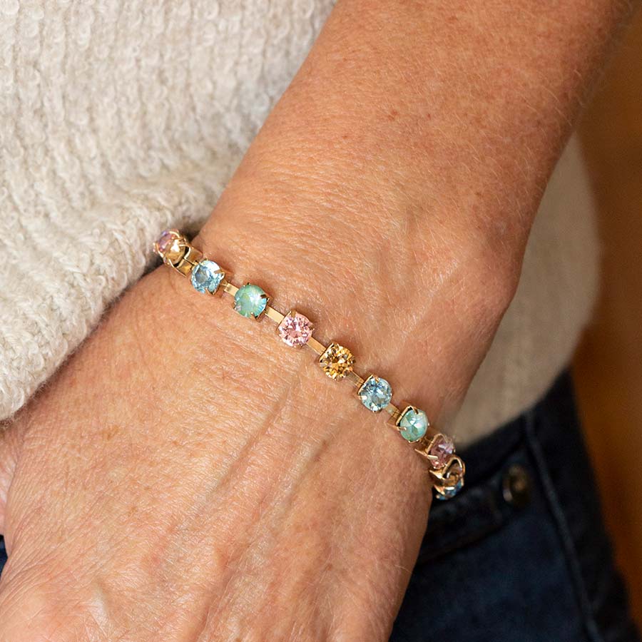 Woman in white sweater with thumb in front pant pocket wearing multi colored crystal gold tone box chain bracelet.