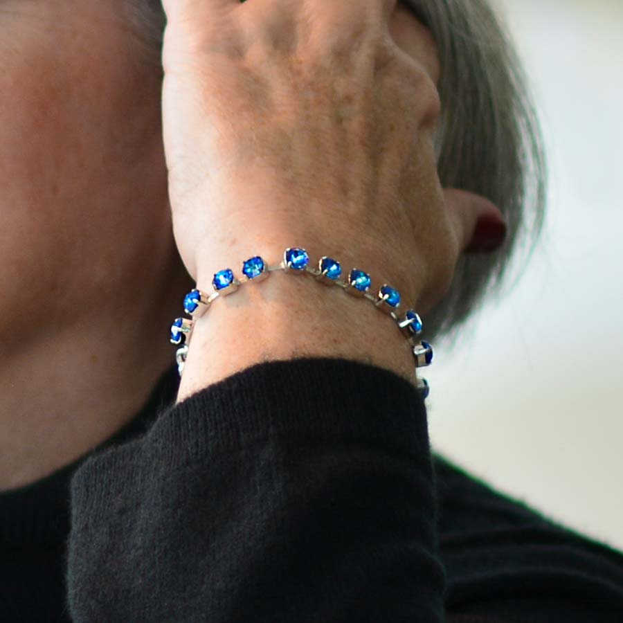 Woman in black top brushing hair from face wearing silver tone box chain bracelet with royal blue crystals.