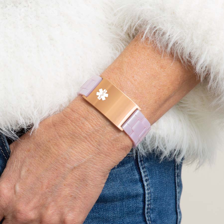 Woman in white sweater wearing lavender resin linked bracelet with attached rose gold tone stainless steel medical ID tag with off-center white medical symbol.