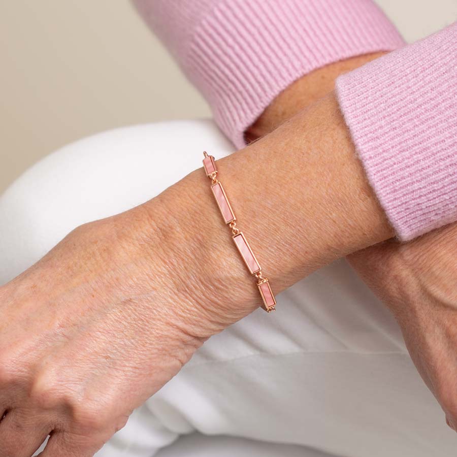 Woman in pink sweater and white pants wearing rose gold tone bar link chain bracelet with blush mother of pearl inlay.