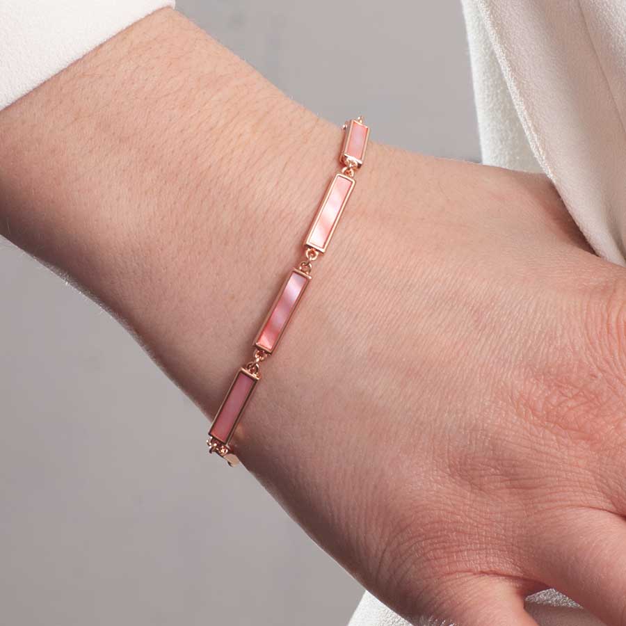 Woman wearing rose gold tone bar link bracelet with pink mother of pearl inlay with hand posed at the hip.