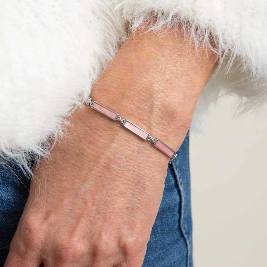 Woman in white sweater and denim wearing silver tone bar link chain bracelet with blush mother of pearl inlay.