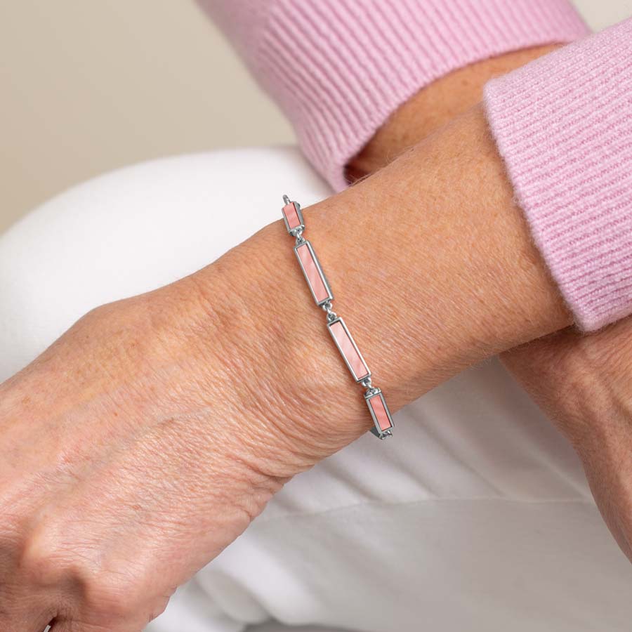 Woman in pink sweater and white pants wearing silver tone bar link chain bracelet with blush mother of pearl inlay.