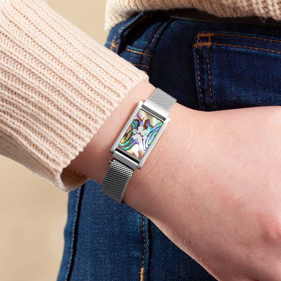 Woman in jeans and sweater wearing stainless steel mesh band bracelet and ID tag with abalone inlay and silver medical symbol.