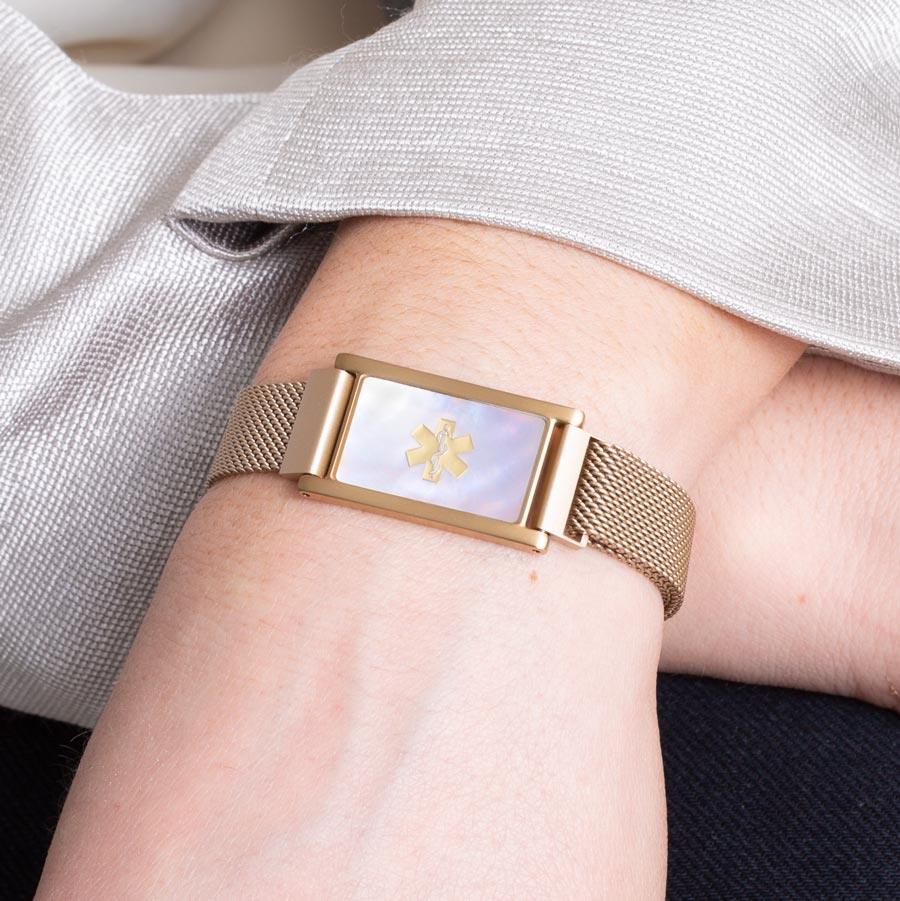 Woman wearing brushed sandstone stainless steel mesh bracelet with gold tone ID tag with natural mother of pearl inlay.