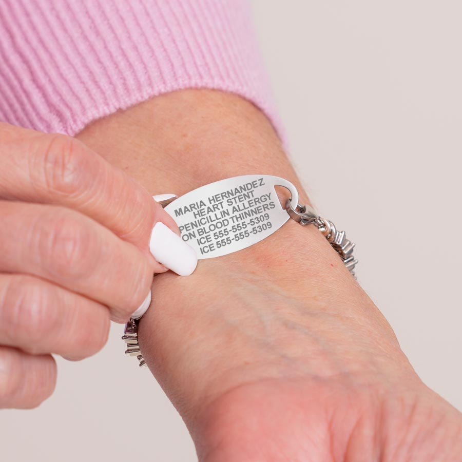 Woman in pink sweater wearing hot pink, magenta, blush, and clear baguette bracelet showing premium laser engraving on stainless steel ID tag.