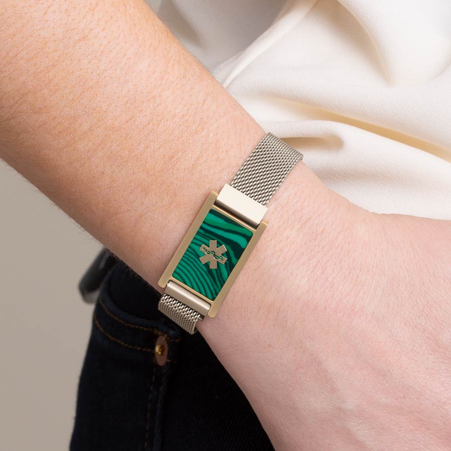 Woman wearing brushed sandstone, stainless steel mesh band with imitation malachite and gold tone medical symbol. 