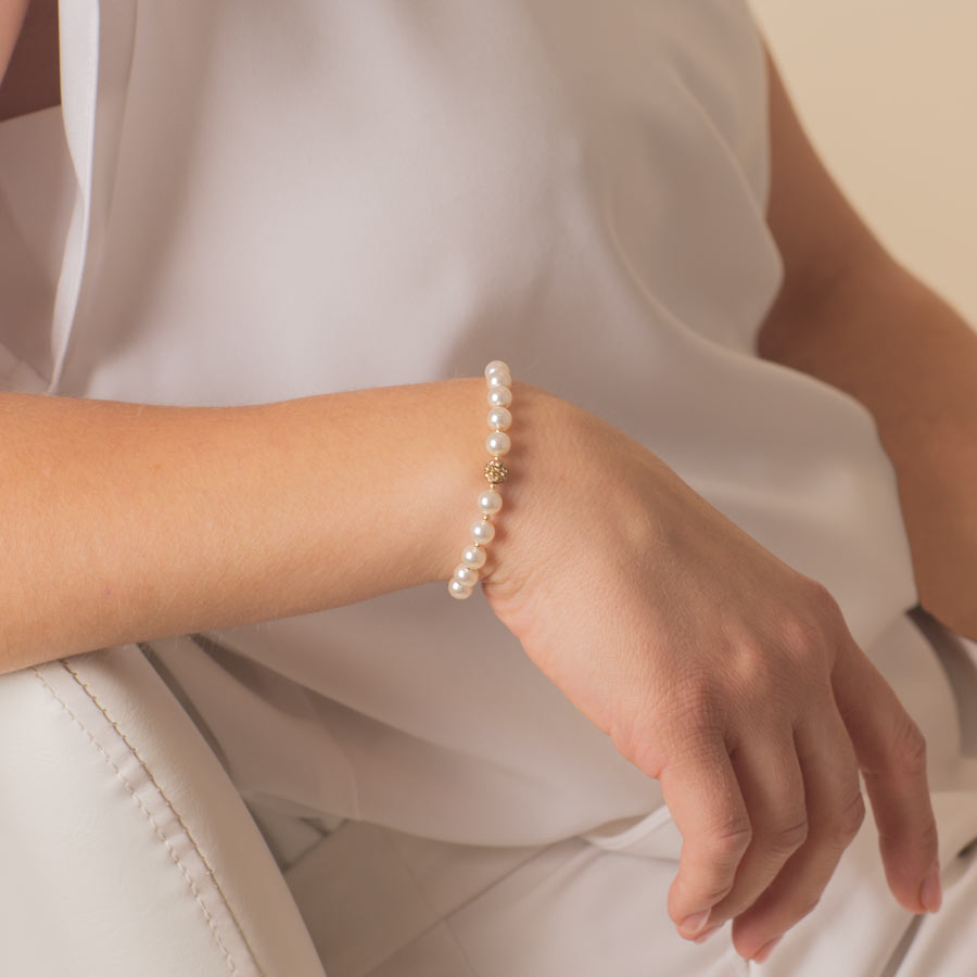 Woman wearing pearl and gold tone stretch medical ID bracelet.